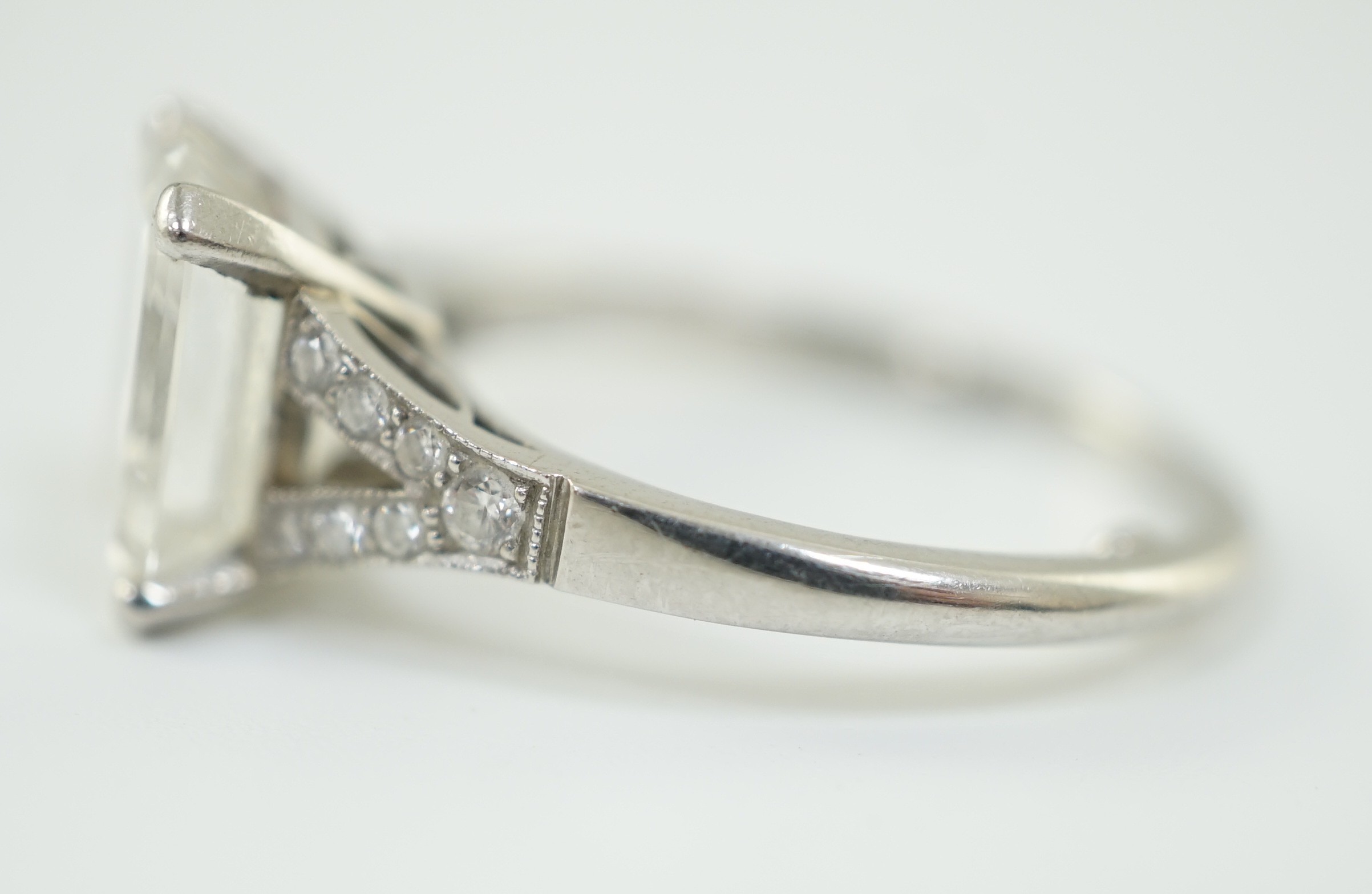 A platinum and single stone emerald cut diamond ring, with brilliant cut diamond set split shoulders